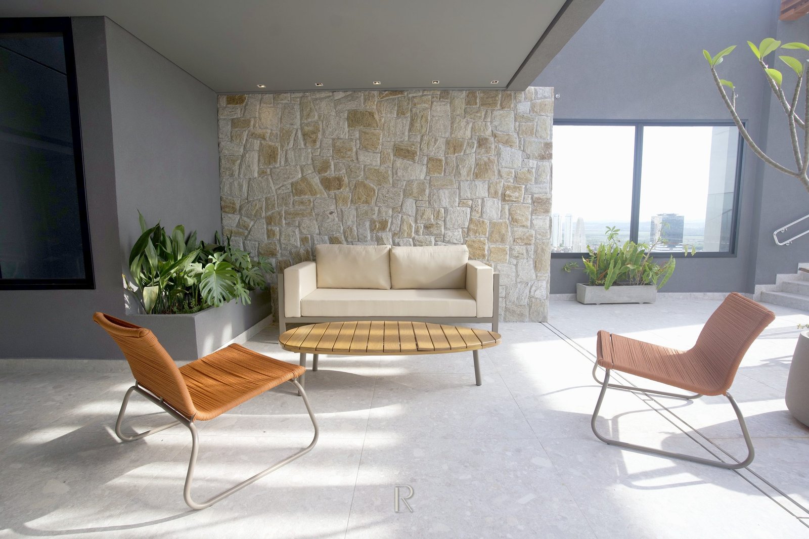 Lounge do edifício, com parede de pedra, poltronas e vista para a cidade