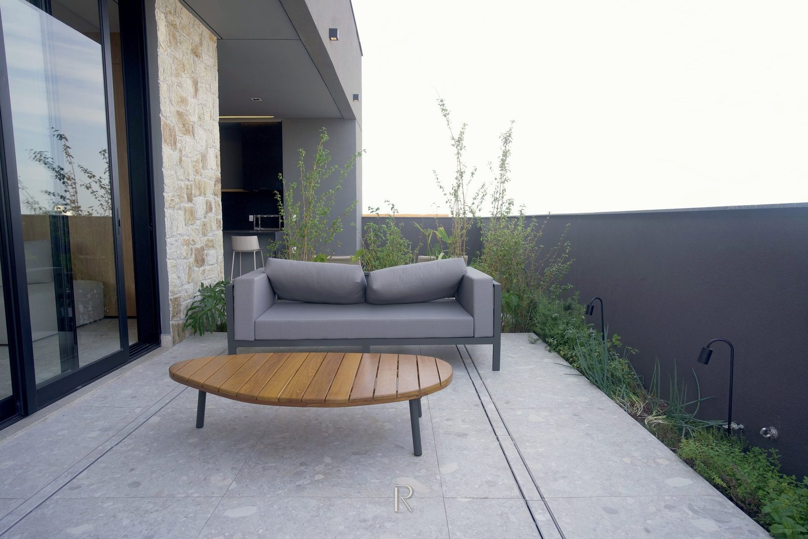 Terraço externo do Matiss, com sofá, mesa de madeira e jardim