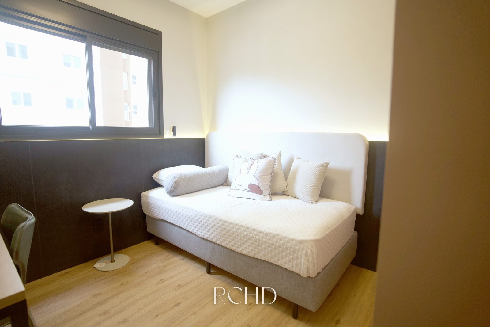 Dormitório do apartamento decorado, com painel de cabeceira e janela à esquerda
